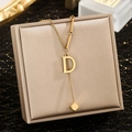 Detailaufnahme der goldenen D-Buchstaben-Halskette mit Würfelquaste auf Schmuckschatulle - Buchstabe D