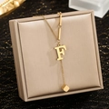 Detail of gold letter F pendant necklace with square tassel on a brushed display box - Letter F