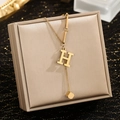 Detail of gold letter H pendant necklace with mini cube tassel on luxury satin - Letter H