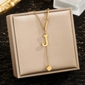 Detail of gold necklace with letter J pendant and cube tassel on jewelry box - Letter J