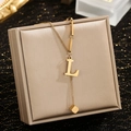 Detail of gold letter L pendant necklace with small cube charm on jewelry box - Letter L