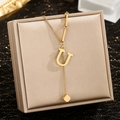 Close-up of golden letter U pendant necklace with square tassel on jewelry box - Letter U