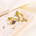 Nahaufnahme asymmetrischer Goldohrringe mit lila Edelstein und weißen Kristallen - Steinbock-Stil (Gold)