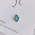 Gros plan d'un pendentif Main de Fatma bleu paon aux bords dorés sur tissu blanc - Cyan Blue