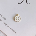 Dettaglio del ciondolo rotondo in smalto bianco con lettera G dorata per gioielli fai da te - Stile G