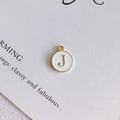 Dettaglio del ciondolo rotondo in smalto bianco con lettera J e bordo dorato per gioielli DIY - Stile J