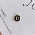 Macro detail of round black enamel letter D charm with gold-plated metal alloy borders - Letter D