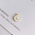 Dettaglio macro di un ciondolo rotondo con lettera K placcato oro e smalto bianco - Stile K