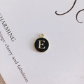 Detail of round black enamel letter E pendant with golden finish for DIY jewelry - Letter E