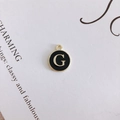 Macro view of a gold-toned alloy charm with black enamel and white letter G detail - Letter G