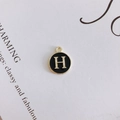 Close-up of a round black enamel pendant featuring a gold letter H on a white card - Letter H