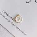 Dettaglio macro del ciondolo con lettera P dorata e smalto bianco su espositore - Stile P