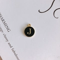 Detailed macro shot of a black enamel round pendant featuring a golden letter J charm - Letter J