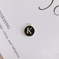 Detail of round black enamel pendant with golden letter K for DIY jewelry projects - Letter K