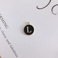 Close-up of a round black enamel letter L charm with a gold metal frame for DIY jewelry - L