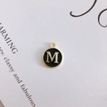 Macro shot of a black enamel round pendant with gold letter M for DIY jewelry making - M