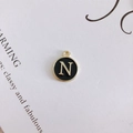 Close-up of a round black enamel letter N pendant with gold-toned alloy edges - Letter N