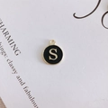 Macro shot of a round black enamel letter S pendant with gold metal edges and hanging loop - S