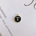 Macro detail of round golden pendant with black enamel letter T for DIY jewelry making - Letter T