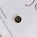 Macro detail of round gold-plated alloy pendant with black enamel and letter U - Letter U