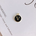 Macro detail of a round black enamel pendant with gold letter V for DIY jewelry making - Letter V