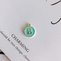 Detalle de un colgante redondo dorado letra B con esmalte azul claro en tarjeta - Letra B