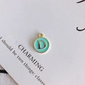 Detalle de un colgante redondo esmaltado con borde dorado y letra D para bisutería DIY - Letra D