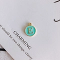 Macro view of mint green enamel letter E round pendant on decorative white card - Letter E