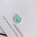 Macro detail of a round green enamel pendant featuring a gold letter K charm component - Letter K