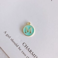 Close-up of a round green enamel pendant with gold letter M for DIY jewelry making - Letter M