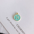 Macro shot of a round gold-rimmed mint green enamel pendant with a golden letter N - Letter N