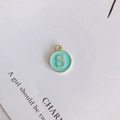 Detailed close-up of a round gold-rimmed light green enamel pendant with letter S engraving - Letter S