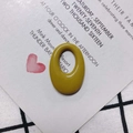Close-up of a mustard yellow oval resin charm on a decorative white card and plaid fabric - Ginger Yellow (5#)