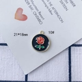 Dettaglio di un ciondolo rosa rossa smaltata 21x18mm con cornice dorata e bordo perlato - Fiore Rosso Foglia Verde Base Nera Bordo Dorato Stile Rotondo (10#)