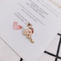 Close-up of pink and gold enamel flamingo earrings on a white invitation card - Pink (Left)