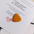 Macro detail of amber resin triangle pendant on a white card with pink heart illustration - Coffee