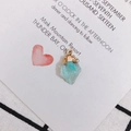Macro shot of an irregular light blue crystal pendant with a gold hook on white card - Transparent Blue