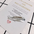 Dettaglio di un fermaglio a goccia d'argento su una cartolina decorativa bianca - 59mm