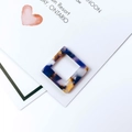Macro shot of colorful marble-textured square acrylic earring charms on a card - Multicolor Abstract Ink Pattern