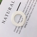Macro detail of a white geometric square ring charm with a smooth matte finish on paper - White