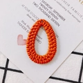 Macro view of orange teardrop woven pendant for DIY jewelry on checkered fabric - Orange