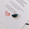 Dettaglio macro di un ciondolo a semicerchio placcato oro con cristallo blu e doppi anellini - Blu navy