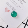 Makroaufnahme eines glatten grünen Achat-Cabochons auf einer weißen Karte und Karo-Stoff - Grün