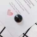 Macro shot of a polished black round glass bead on a white card with heart pattern - Black