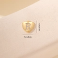Dettaglio macro di un ciondolo a cuore dorato con lettera R in zircone e misura 1cm - Lettera R-Oro
