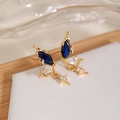 Dettaglio di orecchini a farfalla dorati con zirconi blu e piccoli pendenti a stella - Blu