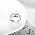 Nahaufnahme eines eleganten gewellten Silberrings mit weißer Perle auf ästhetischem Hintergrund - US 7 / Silber (MSXRJMG748S)