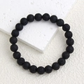 Macro view of 8mm matte black lava stone beads with porous texture on white stone base - Lava Stone Bracelet