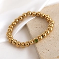 Elastic gold beaded bracelet featuring polished 18K plated beads and a green gemstone - December