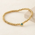 Golden beaded bracelet with a light blue heart zircon on a minimalist stone display - Blue